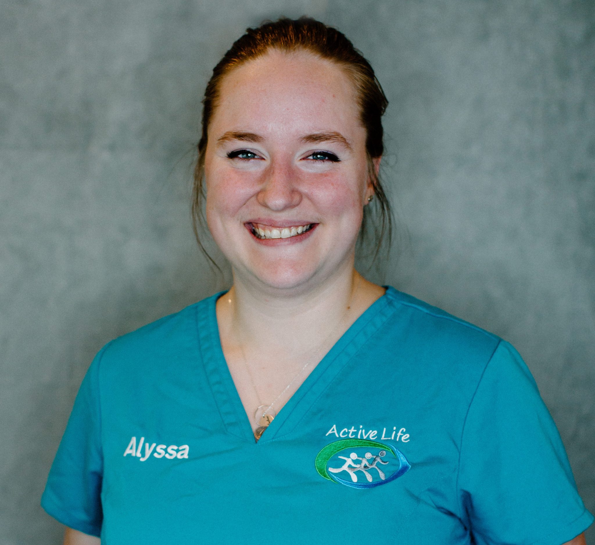 Alyssa Nienhuis smiling in teal scrubs with "Active Life" logo, representing Active Life Chiropractic's commitment to patient care and wellness.