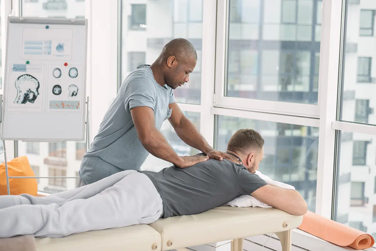 Massage therapist providing therapeutic massage to a client on a treatment table in a bright, modern clinic, emphasizing relaxation and pain relief benefits.