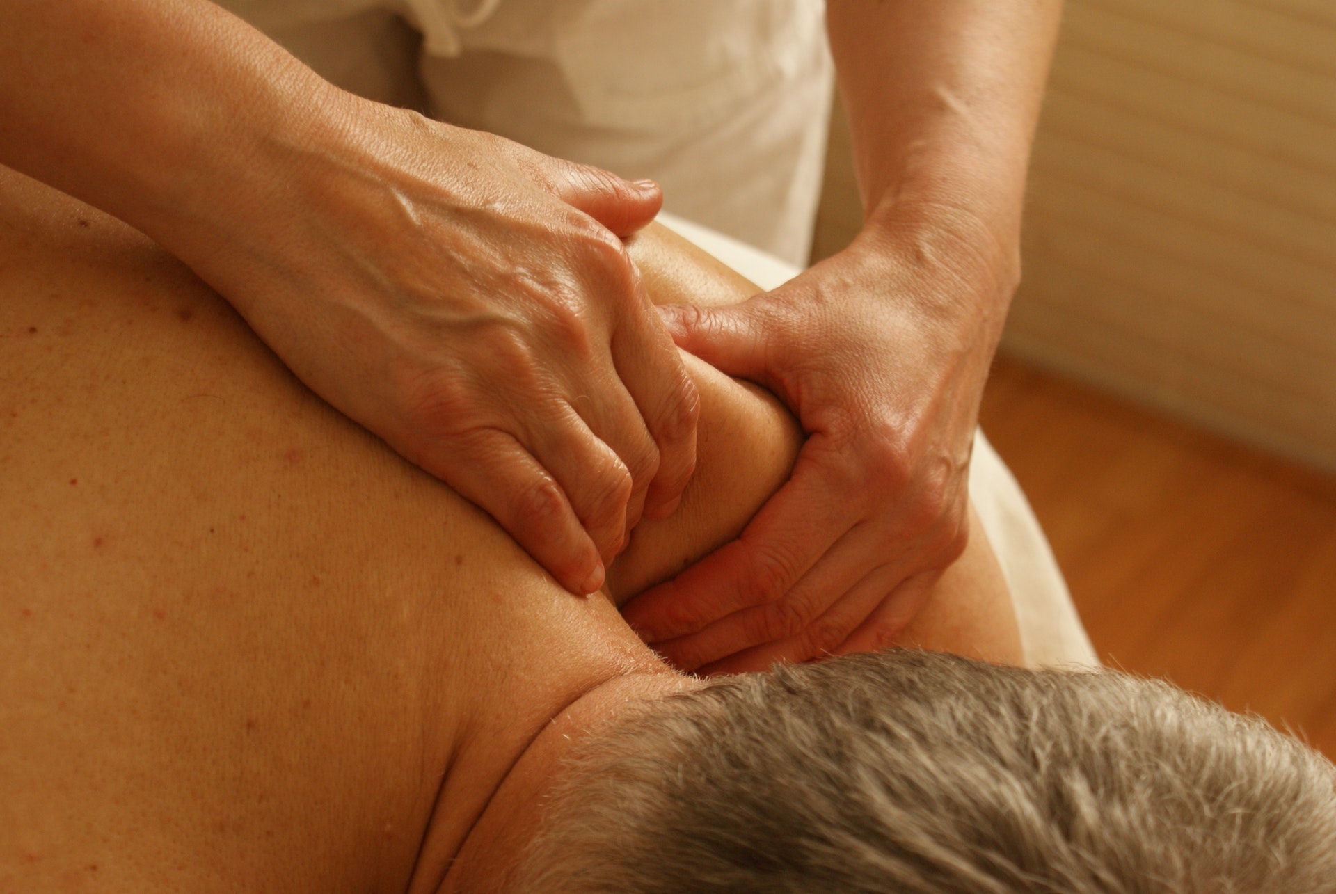 Massage therapist applying deep tissue massage to a client's shoulder and upper back, promoting muscle relaxation and pain relief in a therapeutic setting.