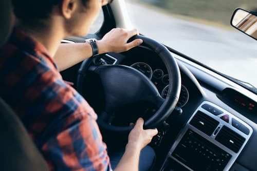 Person driving a car, focusing on the steering wheel, related to car accident injuries and chiropractic care.