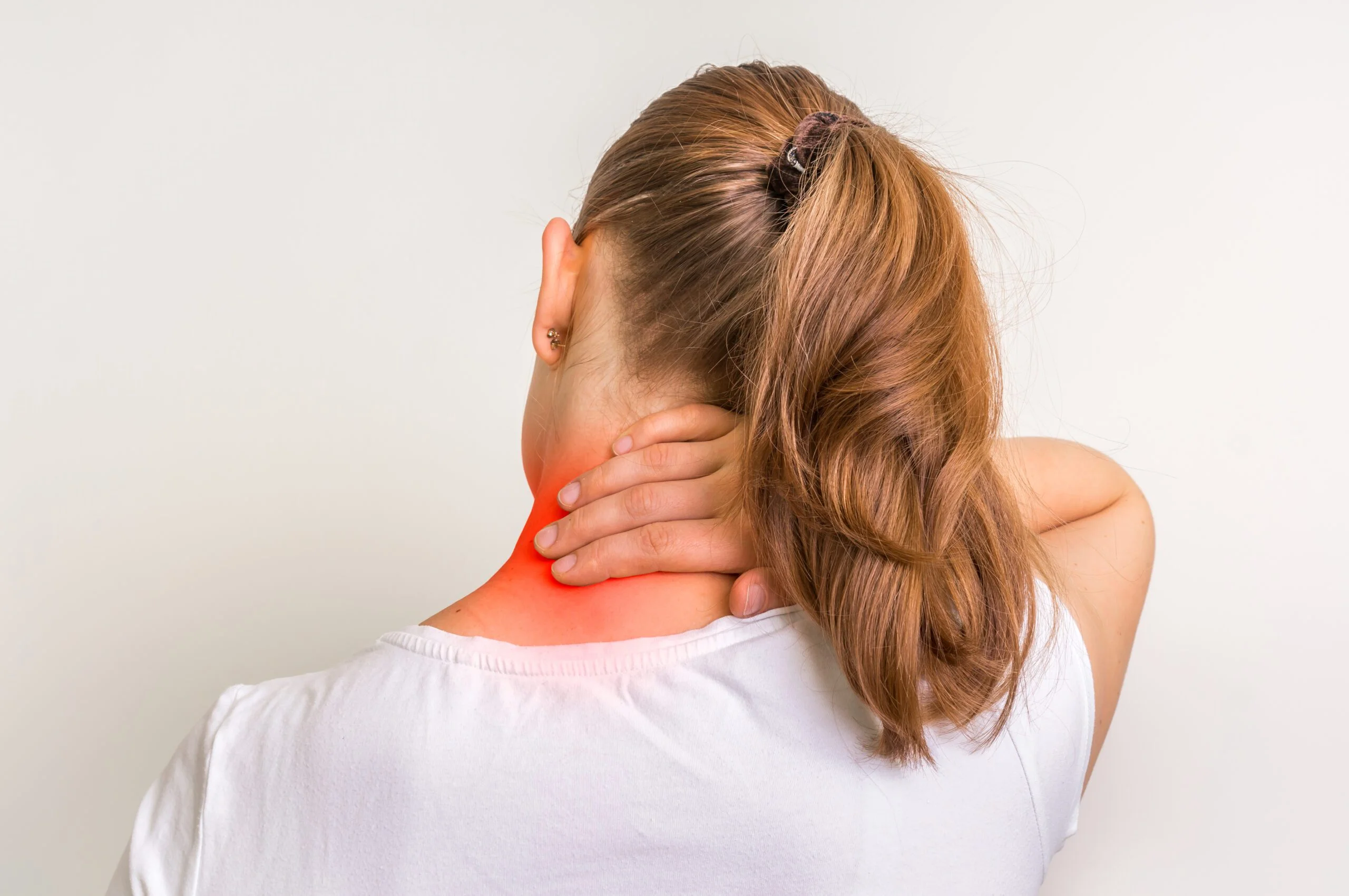 Woman experiencing neck pain, holding her neck with one hand, highlighted area indicating discomfort, white background.