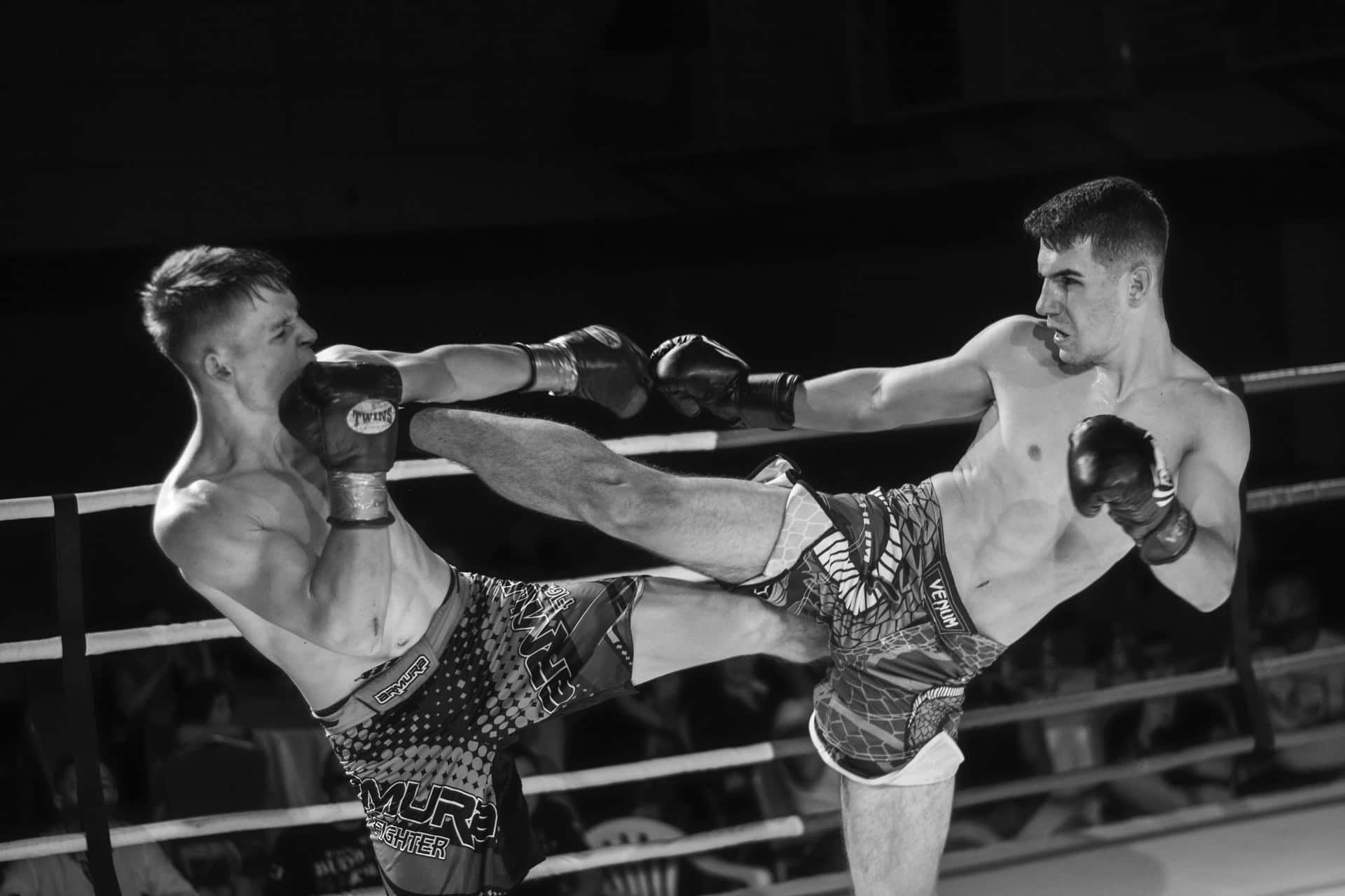 Two male fighters engaged in a kickboxing match, showcasing dynamic movement and athleticism in a ring setting.