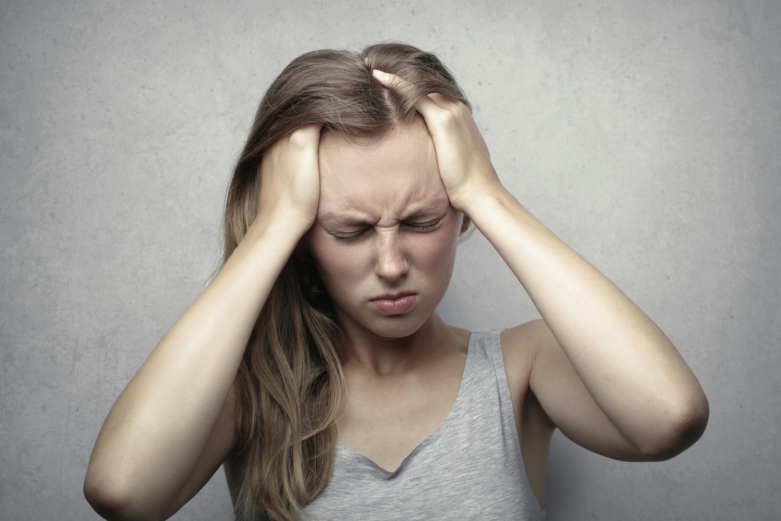 Woman grimacing in pain, holding her head, illustrating severe headache or migraine, relevant to chiropractic care for headache relief.