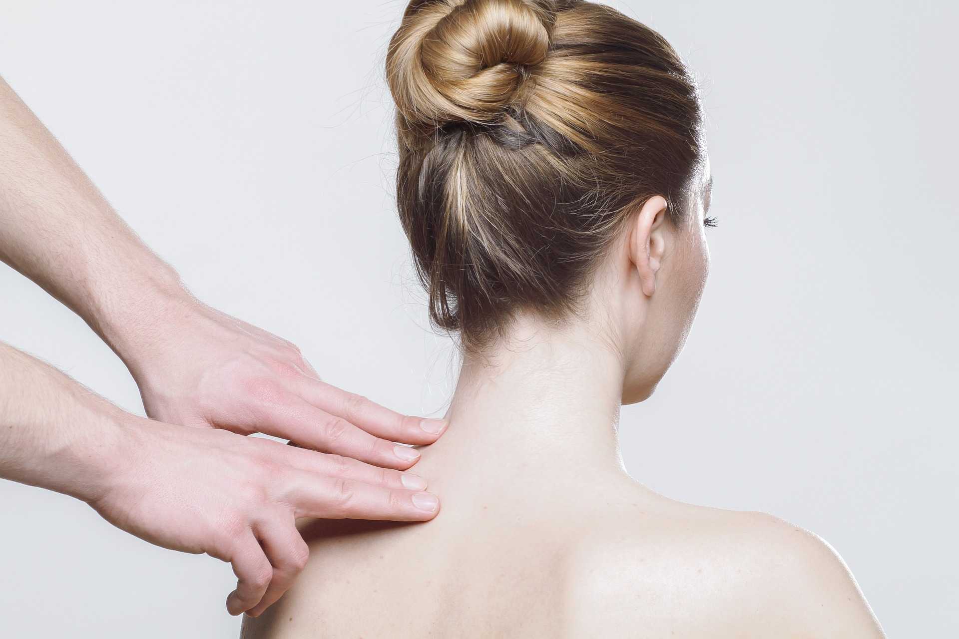 Woman receiving physical therapy for neck pain, focused on whiplash treatment, with therapist's hands applying pressure on the upper back.