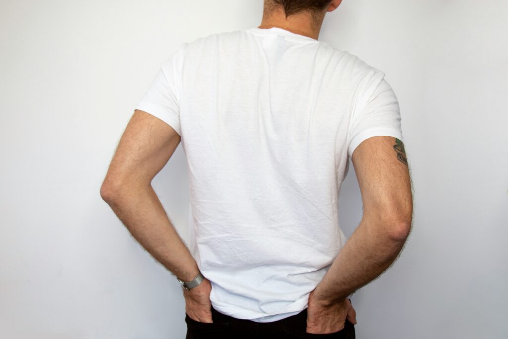 Person in a white t-shirt holding lower back, illustrating lower back pain related to chiropractic care and wellness.