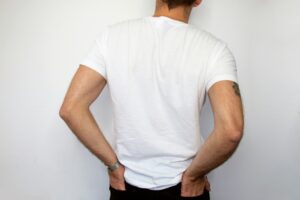 Person in a white t-shirt holding lower back, illustrating back pain relief in chiropractic care context.