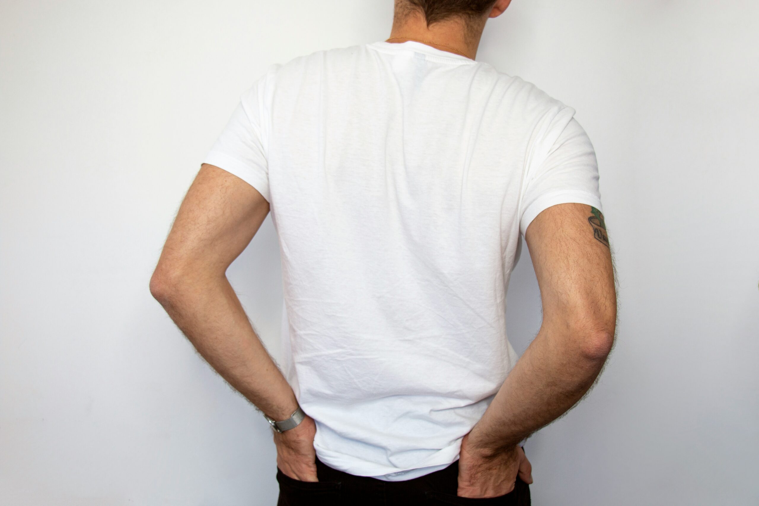 Person in a white t-shirt holding lower back, illustrating the impact of lower back pain on daily life and the need for chiropractic care.